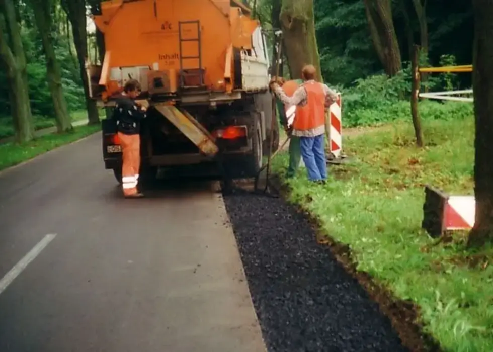 Zwei Arbeiter reparieren den frisch gegossenen Fahrbahnbelag mit einer Schaufel auf einer Landstraße