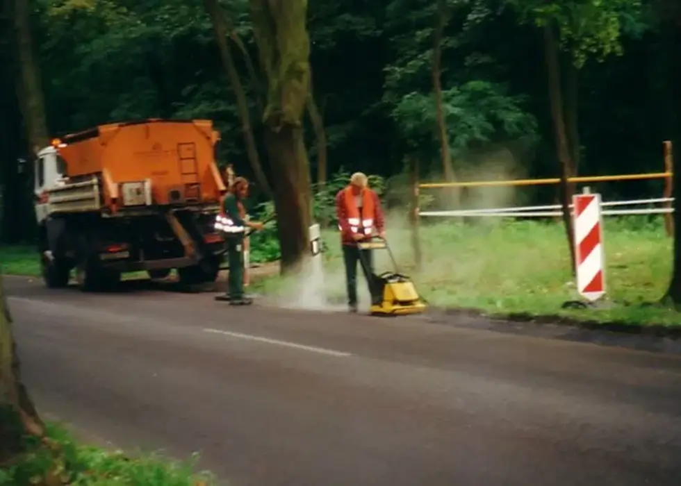 Zwei Arbeiter reparieren den frisch gegossenen Fahrbahnbelag mit einer Walze auf einer Landstraße