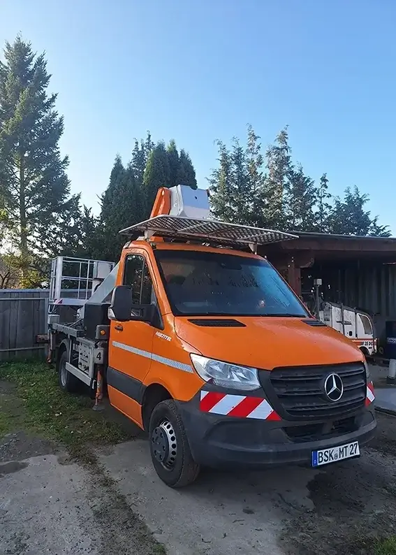 Ein orangenes Bühnenfahrzeug parkt auf einem Bauhof