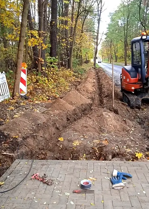 Ein Traktor mit Baggerschaufel gräbt einen Rohgraben aus